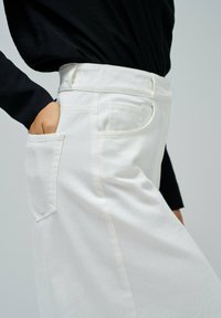 Pantalons blancs taille haute avec une poche latérale, en tissu texturé. Vue partielle mettant en valeur la ceinture et le design épuré.