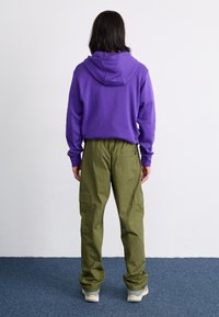 Hanorac mov cu o croială lejeră și buzunar tip kangaroo, asortat cu pantaloni cargo verzi măslinii, cu o croială largă, având buzunare laterale.