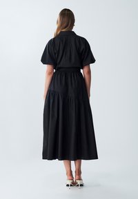 Abito nero con un corpetto aderente e maniche corte a sbuffo, caratterizzato da una vita stretta e una gonna a strati, fluida. Tessuto liscio.