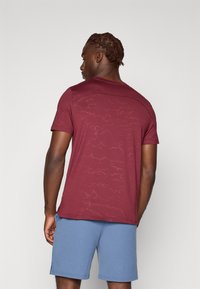Bordeaux kortemouw t-shirt met een subtiel patroon, ronde hals en een getailleerd silhouet, gecombineerd met lichtblauwe shorts.