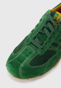 Πράσινο αθλητικό παπούτσι από σουέντ με πάνελ από δίχτυ, στρογγυλή μύτη, ενισχυμένα ραφές και κλείσιμο με κορδόνια, με αντιθετικό κίτρινο πάτο.