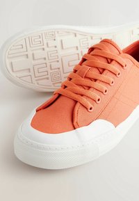 Baskets en toile orange avec embout et semelle en caoutchouc blanc, dotées de lacets plats et de panneaux latéraux texturés. Motif antidérapant en caoutchouc sur la semelle.