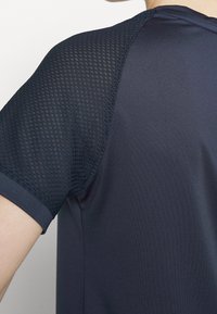 Tmavě námořnický sportovní dres s hladkým tělem a texturovanými síťovinovými rukávy pro prodyšnost. Krátké rukávy s designem kulatého výstřihu.