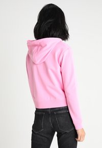 Roze cropped hoodie van zacht materiaal, met een capuchon, geribde mouwen en een nette afwerking. Draagt met donkere jeans, wat een eenvoudige uitstraling toont.