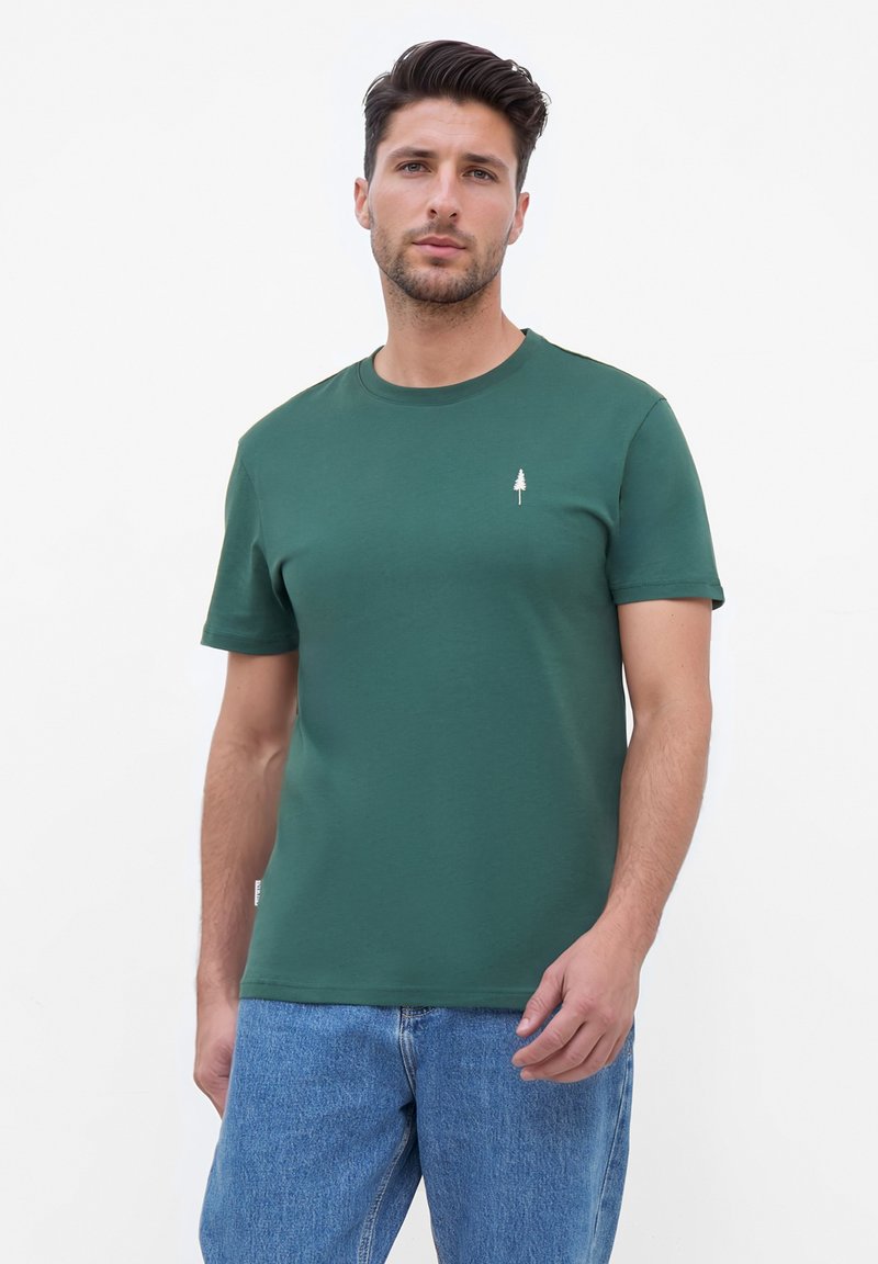 Groene katoenen T-shirt met een ronde halslijn, korte mouwen en een klein wit boomlogo op de borst. Draagt met lichtblauwe spijkerbroek.