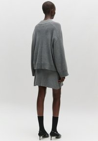 Grauer Strickpullover mit geripptem Saum und Schulternähten. Kombiniert mit einem grauen Rock, schwarzen knielangen Socken und schwarzen Absatzschuhen.