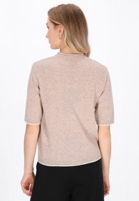 Svetr s krátkým rukávem v světle béžové barvě, vyrobený z měkkého materiálu, s kulatým výstřihem a mírně volným střihem s ribbovaným okrajem.