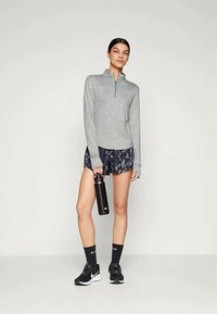 Gray zip-up long-sleeve top, patterned navy shorts, black water bottle, black sneakers, and dark socks in a standing pose.