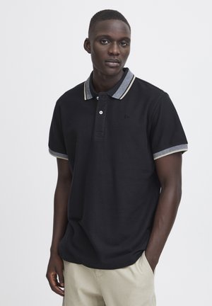 Polo noir avec un col texturé en marine et crème, patte de boutonnage à trois boutons, et manches courtes avec des finitions contrastées. Détail de logo subtil.