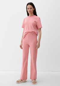 Rosa kurzärmliges Oberteil und passende weit ausgestellte Pants mit einem strukturierten gepunkteten Muster. Getragen mit hellen Sandalen, vor einem weißen Hintergrund.