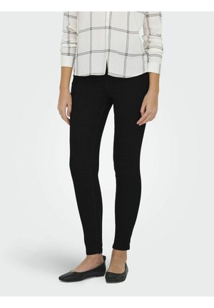 Svarte skinny jeans laget av en elastisk bomullsmiks, med en glatt tekstur og en klassisk passform, sammen med svarte flate sko og en rutete skjorte.