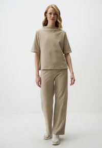 Beige ribbed knit outfit featuring a short-sleeve top with a high neckline and wide-legged pants, paired with light sneakers.