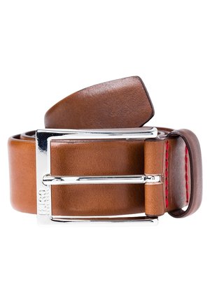 Brązowy skórzany pasek z srebrną prostokątną klamrą i czerwonym przeszyciem w pobliżu pętli, zwinięty na białym tle.