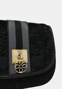 Borsa in tessuto trapuntato nera con tracolla a righe grigie e nere, dotata di una chiusura dorata incisa "V°73" e un charm rotondo decorativo dorato.