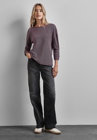 Langarmige bordeaux gestreepte top gecombineerd met ruime zwarte jeans en witte sneakers. De top heeft een bootnecklijn en een gestructureerde stof.