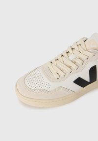 Sneaker in pelle e suede beige, con una punta forata, lacci beige, logo blu scuro e una suola in gomma testurizzata.