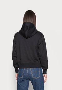 Sudadera recortada negra con capucha ajustable y puños acanalados. Hecha de un tejido suave, presenta una textura lisa y un diseño sencillo.
