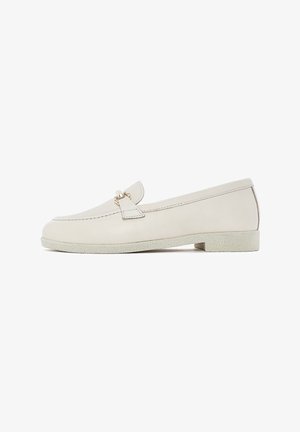 Mocassins en cuir beige avec un bout arrondi, semelle plate et un petit nœud décoratif. Présentent des coutures minimales et une semelle texturée.