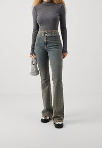 Höga ljusblå jeans med en lätt blekning, med knappgylf, fickor och utsvängda ben, i kombination med en figurnära grå långärmad topp.