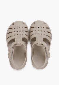 Sandalias de plástico beige con un diseño de tiras trenzadas y una correa trasera ajustable. Plantilla texturizada para un mejor agarre y comodidad.