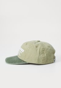 Green cotton baseball cap with a textured light green crown and darker green visor, featuring white embroidered text on the front.