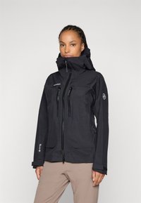 Black waterproof jacket with zippered pockets, high collar, adjustable hood, and logo on sleeve; designed for outdoor activities.