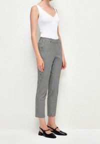 Pantalon à carreaux noirs et blancs à coupe ajustée avec des poches avant. Assorti à un débardeur blanc moulant et des chaussures à bride arrière noires.