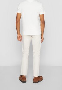 Weißes T-Shirt mit kurzen Ärmeln, kombiniert mit hellbeigen Hosen und braunen Schuhen. Das Outfit hat einen lockeren Schnitt und ein einfaches Design.