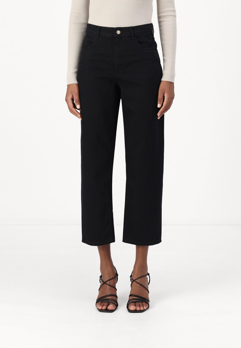 Mustad laiad teksapüksid, valmistatud denimkudumist, kõrge talje ja nööbitusega, nelja taskuga. Ühendatud õhukeste rihmadega mustade sandaalidega.