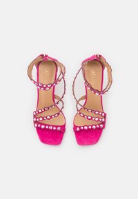 Fuksia vaaleanpunaiset korkeakorkoiset sandaalit, joissa on mokkanahkainen pinta, useita strap-muotoiluja ja jalokivikoristeet edessä ja sivuilla.