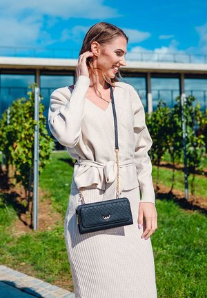 Light beige, long-sleeve wrap sweater with a tie at the waist, paired with a ribbed beige skirt. A small black quilted crossbody bag with a logo.