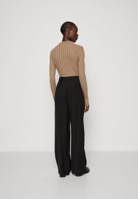 Beige ribbet langærmet top sammen med højtaljede sorte vide bukser, der har en ren, glat tekstur og minimalistisk design.