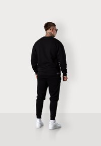 Sweat-shirt noir et joggings en mélange de coton, dotés de poignets côtelés et d'un détail logo subtil sur la taille, associés à des baskets blanches.