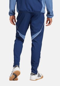 Koninklijk blauwe sportbroeken met lichtblauwe accenten, taps toelopende pijpen en zijritsen, gecombineerd met witte sneakers.