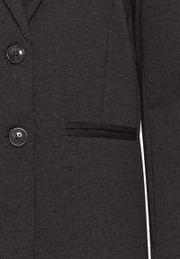 Acercamiento a un blazer gris oscuro que muestra dos botones negros, solapa con muesca y un bolsillo horizontal con detalle de ribete en el lado derecho.