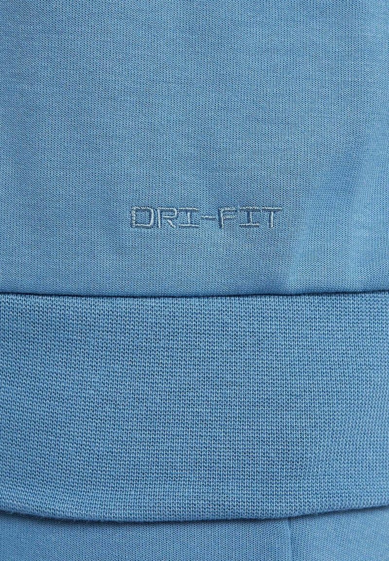 Helles blaues Dri-FIT-Gewebe mit strukturiertem Strick. Verfügt über das gestickte "Dri-FIT"-Logo in einem etwas dunkleren Blau, das sich nahe dem unteren Rand befindet.