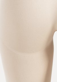 Beige naadloze legging met een gladde textuur, matte afwerking en subtiel geribbelde details langs de tailleband en de binnenkant van de dijen.