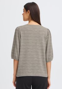Blouse à carreaux gris et beige avec des manches courtes bouffantes. Tissu léger avec une finition texturée. Coupe droite avec un col arrondi.