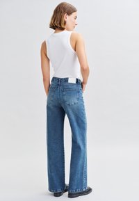 Jean en denim bleu taille haute avec une jambe droite, présentant un design de poche arrière et une étiquette blanche sur la taille.