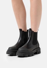 Černé Chelsea boty s hladkým koženým svrškem, elastickými bočními panely a silnou texturovanou podrážkou s designem zubů na okraji.