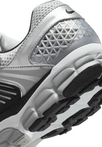 Sive in srebrna športna obutev z teksturiranim zgornjim delom, mrežnimi paneli in gumijastim podplatom s izrazitimi vzorci za oprijem.