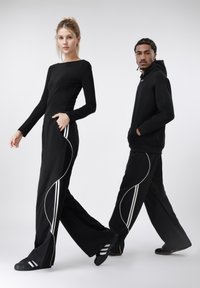 Fekete hosszú ujjú felső és fekete nadrág fehér csíkokkal. A nadrág hullámos mintával díszített. Mindketten sötét lábbelit viselnek, minimalista megjelenést kölcsönözve.