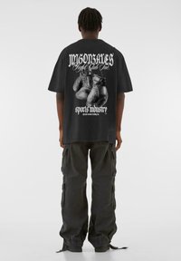 Sort bomulds t-shirt med grafik af boksehandsker og tekst på ryggen, parret med mørke cargo-bukser med sidelommer og snore.