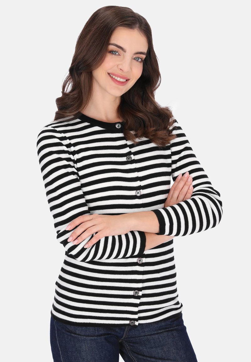 Zwart-wit gestreept vest met een geribbelde textuur, knoopsluiting aan de voorkant en lange mouwen. Gestyled met een donkere spijkerbroek.