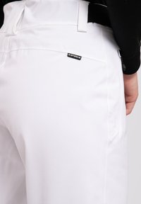 Witte broek met een gladde textuur, voorzien van een zichtbaar logo-patch, ritszakdetails en een getailleerde pasvorm in de taille.