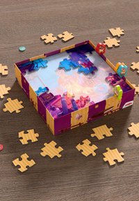 Buntes Puzzle mit einer lila Box, die Figuren zeigt, umgeben von Holzpuzzlestücken in verschiedenen Formen und Designs auf einer Holzoberfläche.