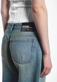 Ljusblå denimjeans med hög midja, utrustade med klassiska bakfickor och en svart märkesetikett med texten "DRDENIM" sydd vid midjan.