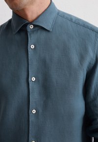 Knapp-up skjorta i mjuk, strukturerad linne i en djup teal-färg. Har en klassisk krage och sex ljusa knappar fram.