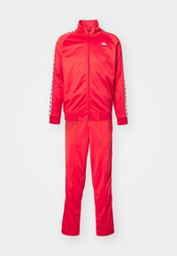 Survêtement rouge en polyester brillant, comprenant une veste zippée sur toute la longueur et un pantalon assorti, avec des détails rayés contrastants sur les manches.