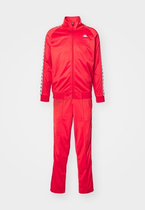 Puna treeningkostüüm, mis on valmistatud läikivast polüestrist, sisaldab täispika tõmbluku ja vastandlike triibuliste detailidega jakki ning sobivaid pükse.